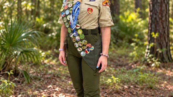 Yaffa Zippin in Scout uniform with a merit badge sash, standing on a wooded trail