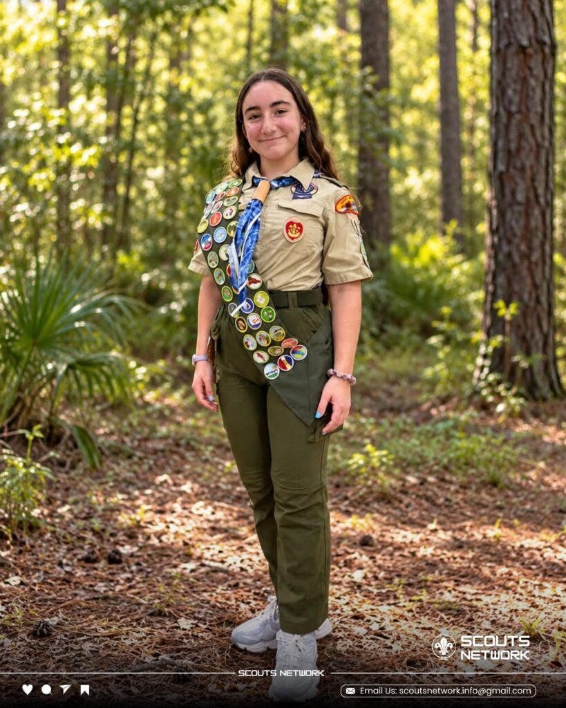 Yaffa Zippin in Scout uniform with a merit badge sash, standing on a wooded trail